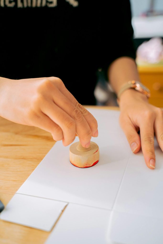 Other Image Close-up of a person using a wooden stamp on white paper indoors.