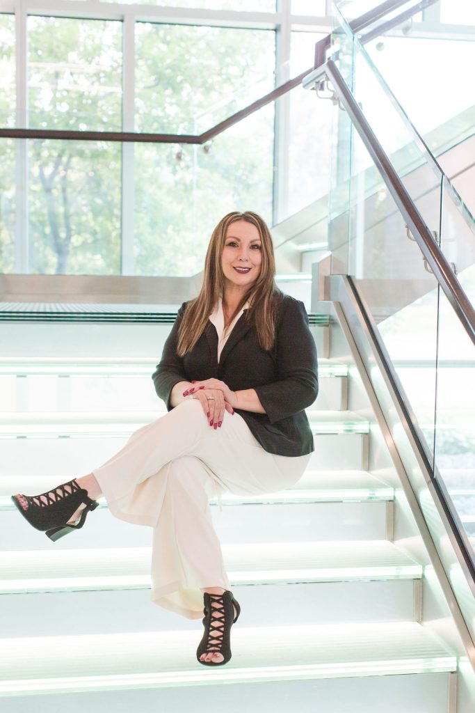 Meet Elizabeth Leyva, Certified Mobile Notary and Signing Agent Elizabeth Leyva, mobile notary and certified signing agent, seated on a modern glass staircase in professional business attire.